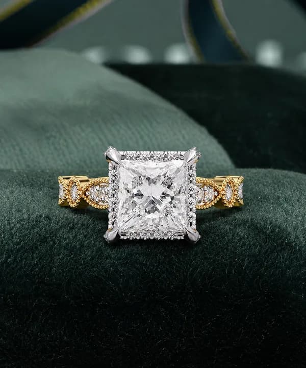 Princess cut lab grown diamond halo engagement ring with vintage band in yellow gold resting on green velvet
