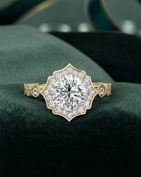 Cushion cut lab grown diamond vintage floral halo engagement ring in yellow gold resting on green velvet