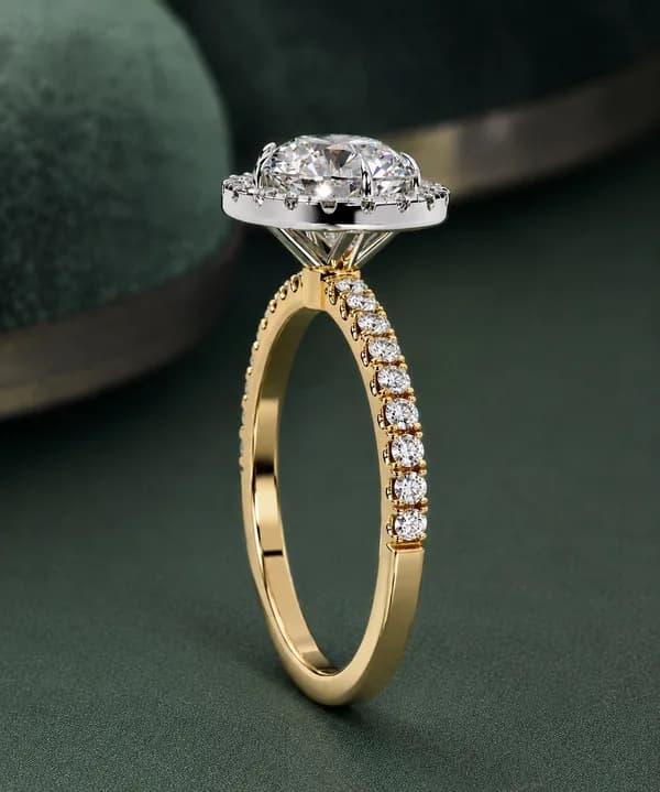 Round lab grown diamond halo engagement ring with pavé band in yellow gold, side view on green velvet