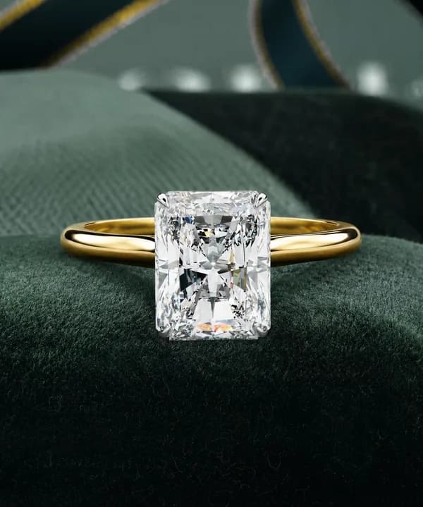 Radiant cut lab grown diamond cathedral solitaire engagement ring in yellow gold resting on green velvet