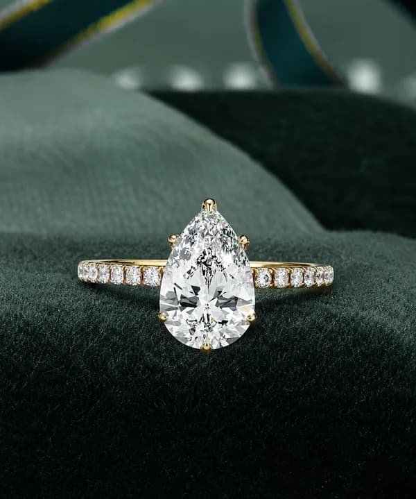 Pear cut lab grown diamond hidden halo engagement ring with pavé band in yellow gold resting on green velvet