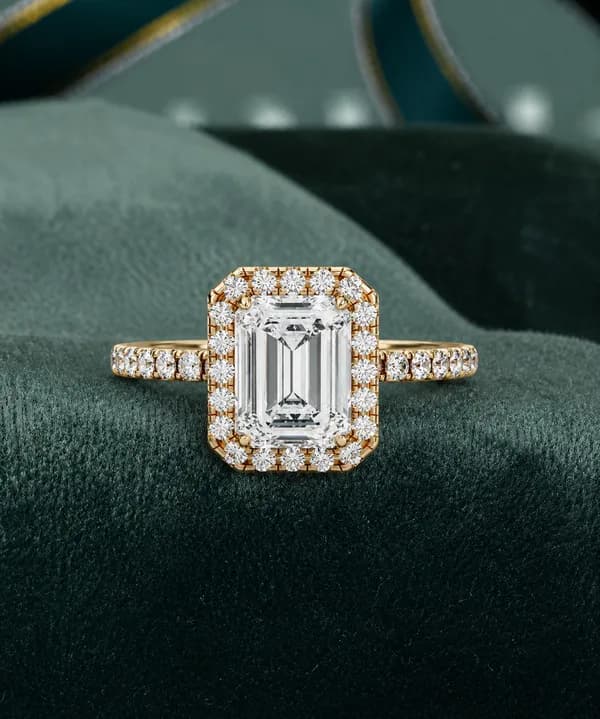 Emerald cut lab grown diamond halo pavé engagement ring in yellow gold on green velvet