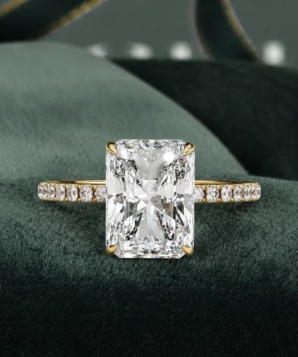 Radiant cut lab grown diamond hidden halo pavé engagement ring in yellow gold resting on a green velvet cushion