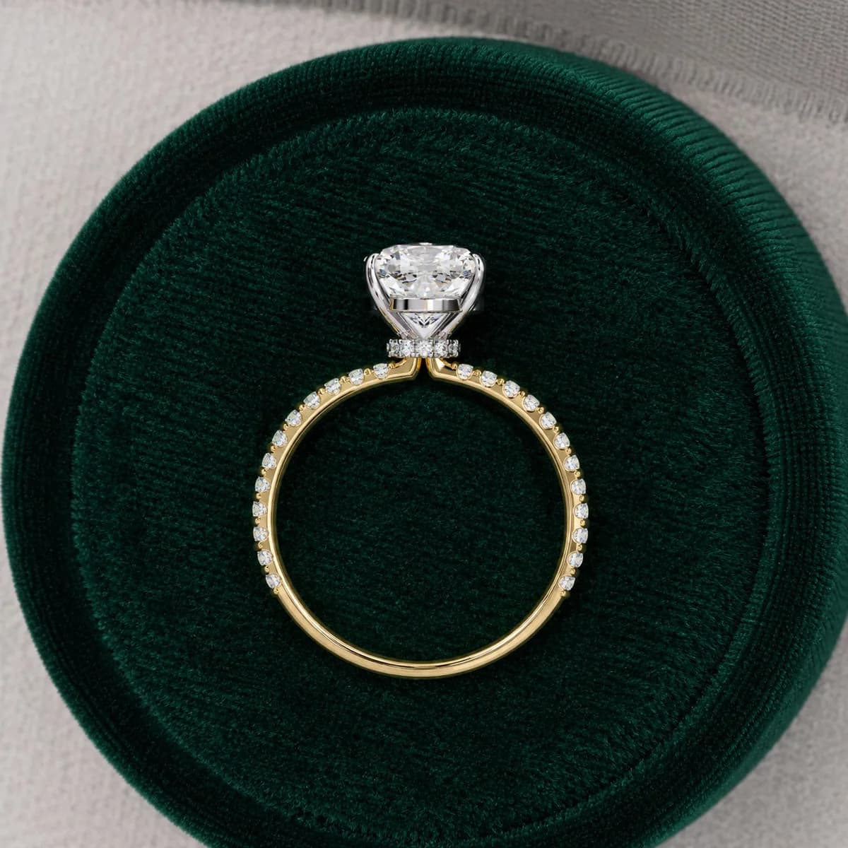 Cushion cut lab grown diamond hidden halo engagement ring with pavé band in yellow gold standing in a green velvet ring box