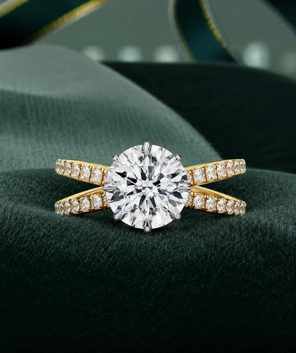 Round lab grown diamond criss-cross pavé engagement ring in yellow gold resting on green velvet