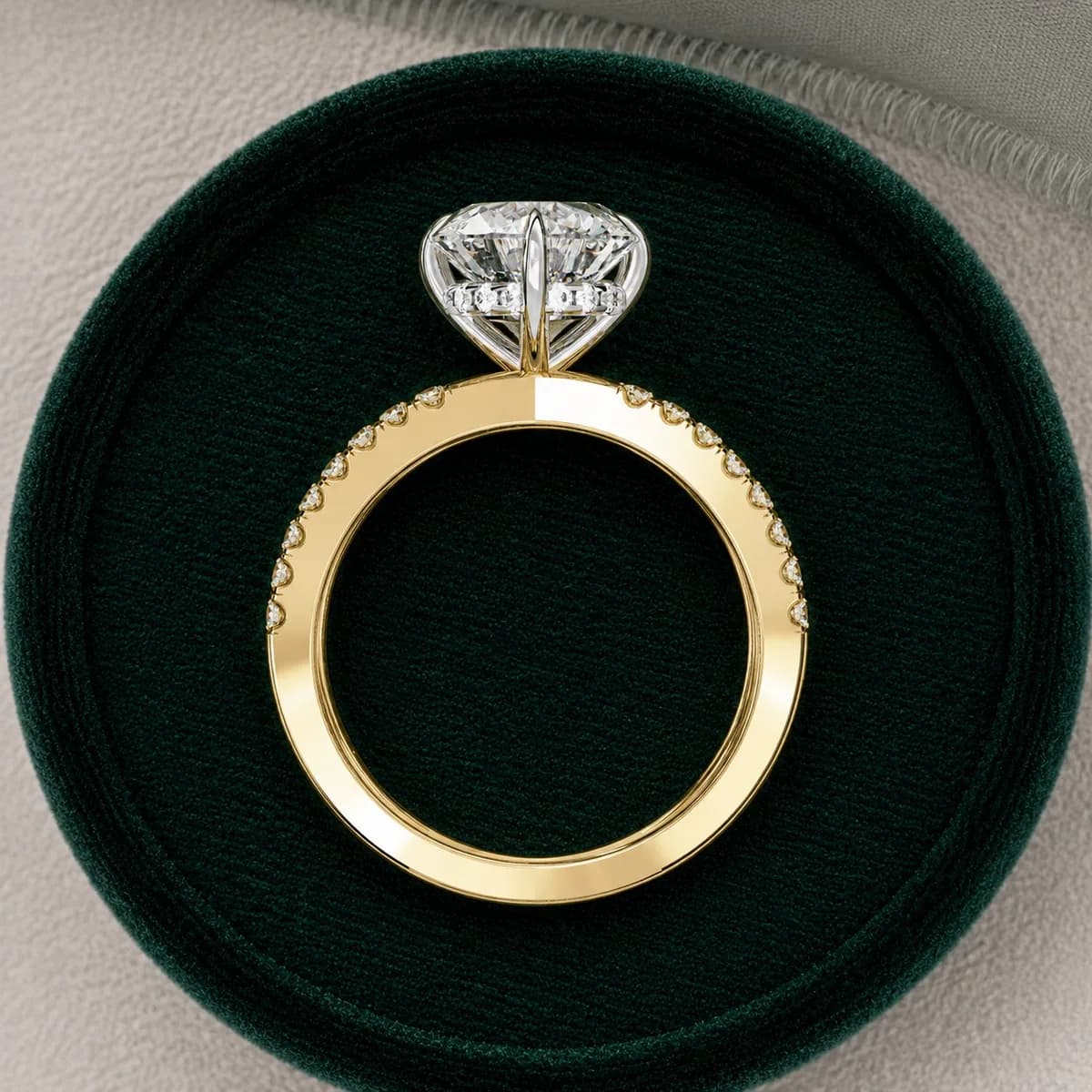 Round lab grown diamond criss-cross pavé engagement ring in yellow gold standing in a green velvet ring box