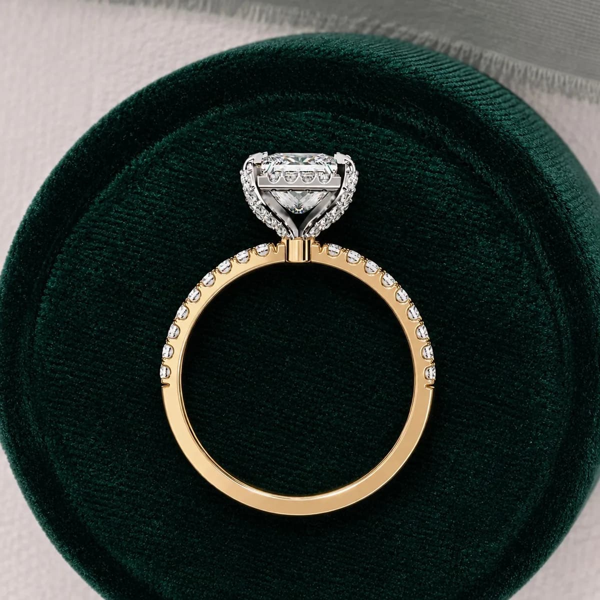 Princess cut lab grown diamond low halo engagement ring with pavé band in yellow gold standing in a green velvet ring box