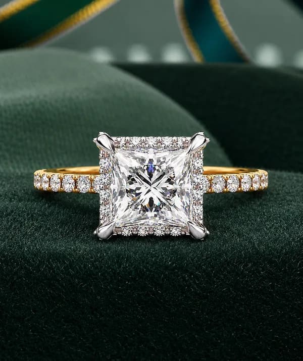 Princess cut lab grown diamond low halo engagement ring with pavé band in yellow gold resting on green velvet